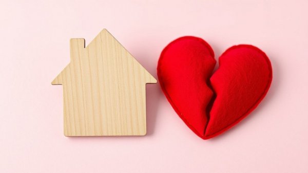 Wooden house and broken heart on pink background, symbolizing catfishing in real estate marketing.