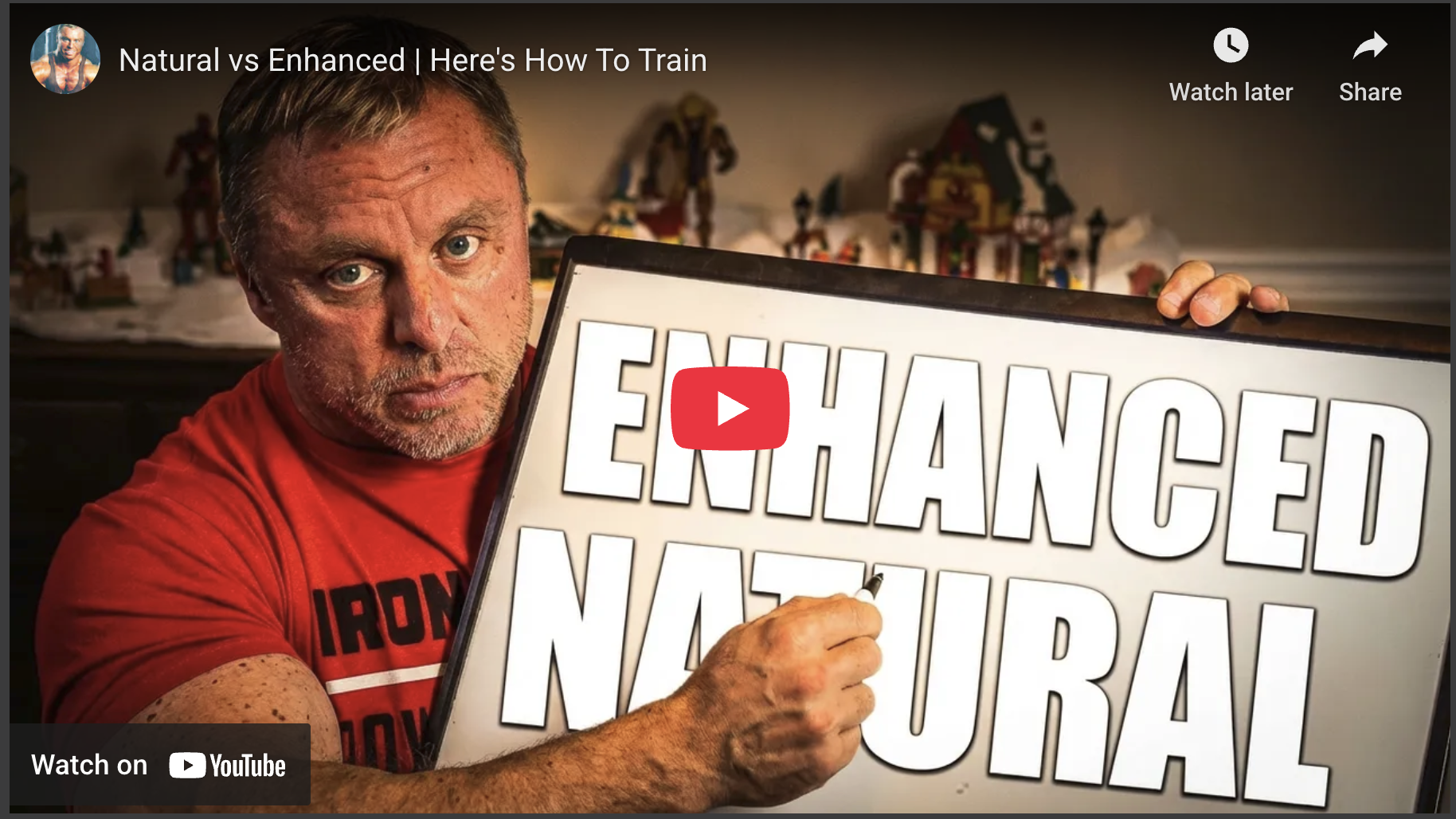 Muscular man with 'Enhanced Natural' sign, indoors, warm lighting.
