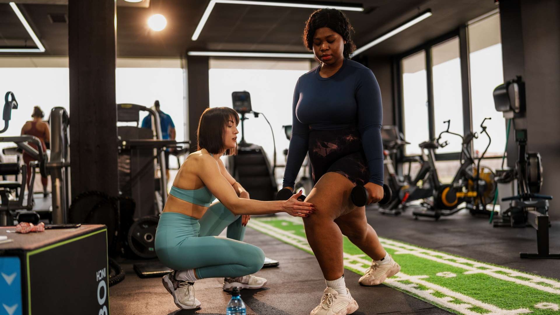 Fit young woman showcasing muscle growth during leg day squat in a minimalist gym.