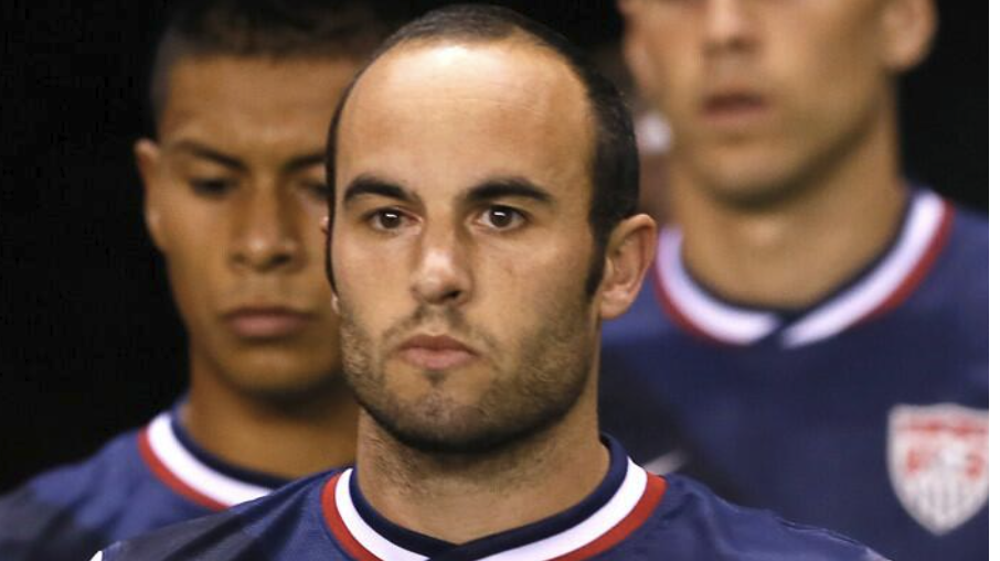 Landon Donovan signing books at an indoor event, smiling.