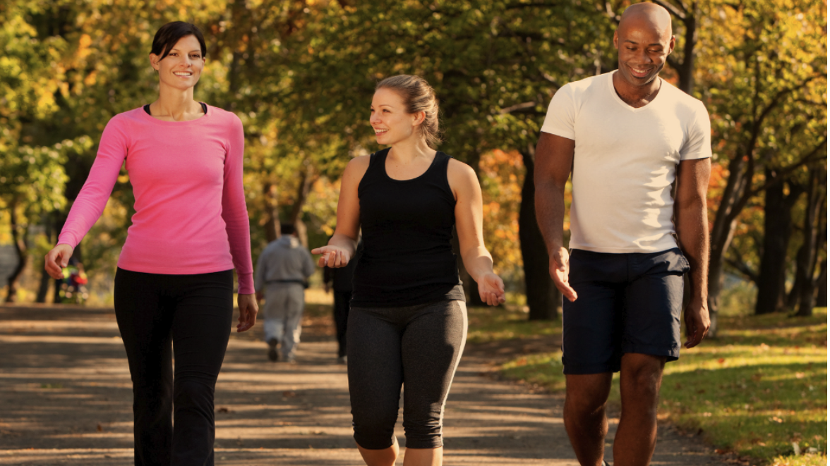 Smiling middle-aged person in athletic gear, striding confidently in green setting.