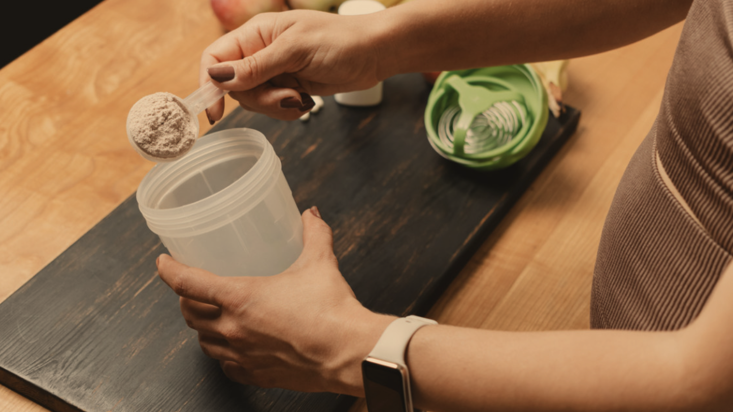 Collagen powder being added to coffee beside a collagen jar and healthy breakfast items on a wooden table.
