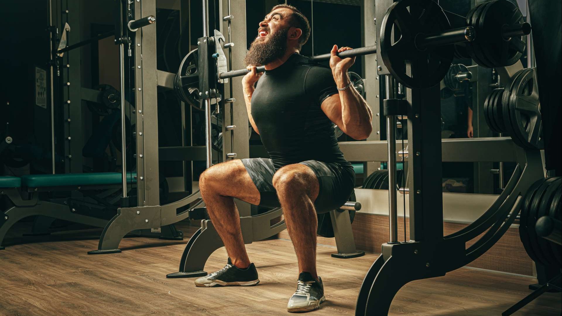 Muscular man performing Smith Machine Leg Raises in gym.