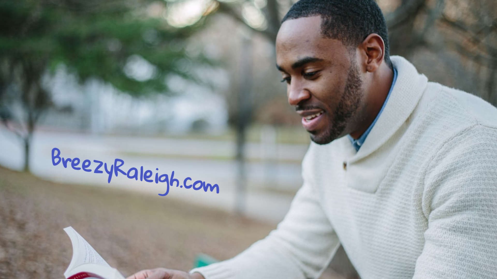 Man with white sweater outside reading book