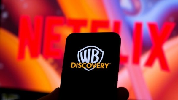 Smartphone with Warner Bros logo and Netflix logo in background symbolizing merger and acquisition.