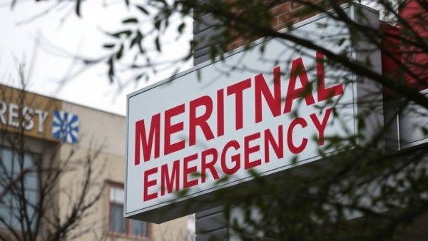 Hospital emergency sign partially obscured by branches