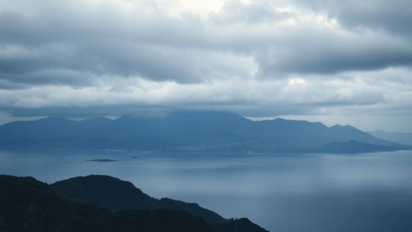 Scenic sea view with mountain and clouds near urban coastline.
