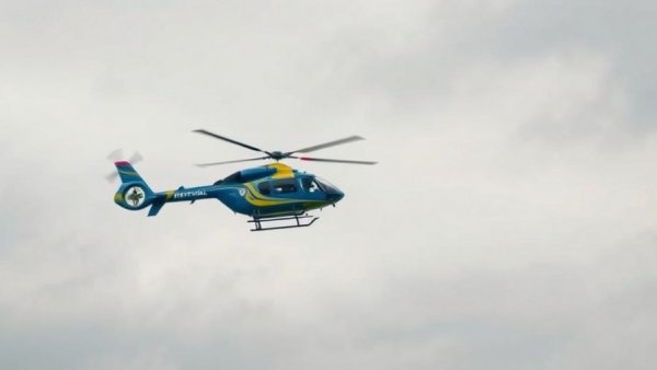 Blue and yellow medical helicopter hovering mid-air on a cloudy day.