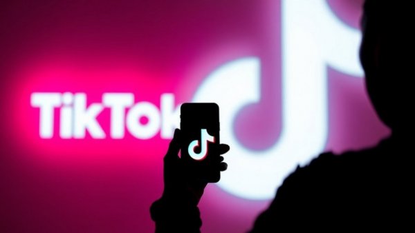 Silhouette with phone displaying TikTok logo, large logo in background.