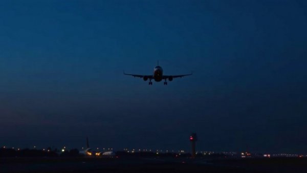 Airbus A320 ascending at dusk over airport with glowing lights.