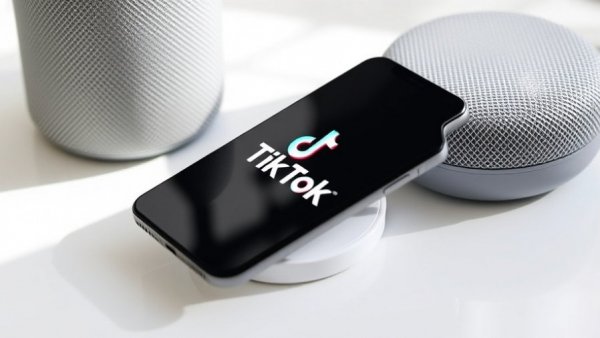 Smartphone showing TikTok logo on wireless charger next to speaker.