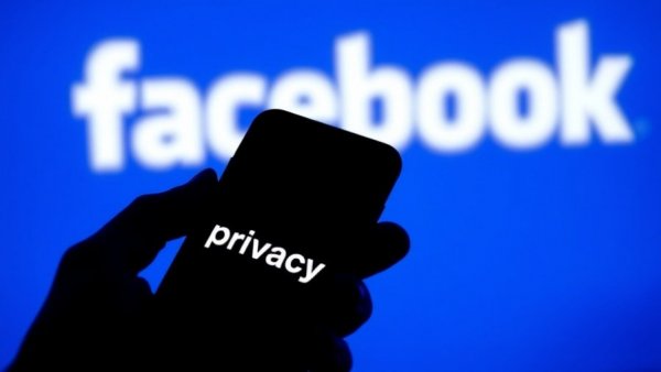 Smartphone held in hand with privacy on screen over Facebook logo background.
