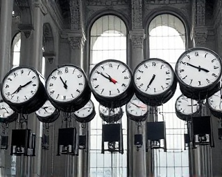 commanding time control, assertive, synchronizing a cascade of analogue clocks, photorealistic, in a grand hall with marble and glass architecture, highly detailed, pendulums swinging in unison, crystal clear precision, black and white with subtle reds, diffuse sunlight through tall windows, shot with a 70-200mm zoom lens.