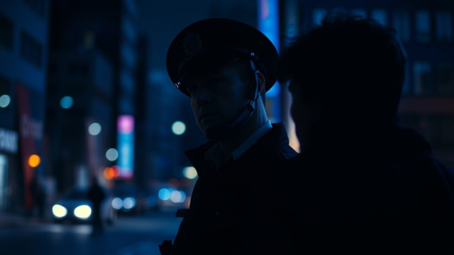 Police officer at night scene with dark, somber lighting.