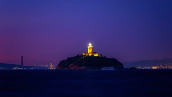 Alcatraz Island lit up during a night tour with glowing lighthouse.