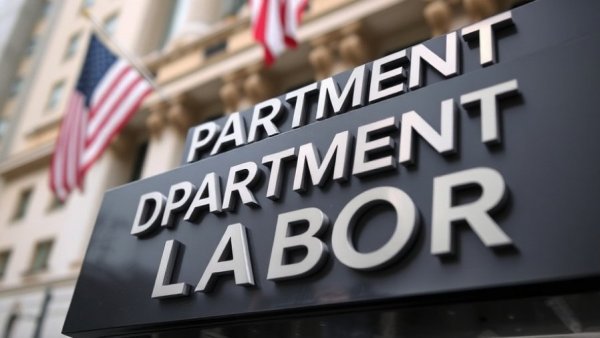 Department of Labor building sign with blurred background, American flag visible.