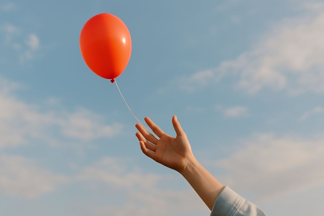 Hand releasing balloon, representing letting go of control in anxiety management.