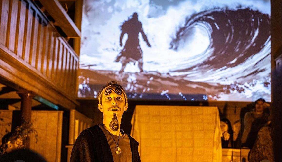 Foinse performer in spiral face paint in front of a projected wave
