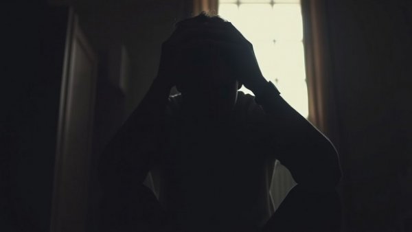 Contemplative man in silhouette, representing depression and introspection, against bright window.