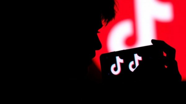 Silhouette with smartphone in front of TikTok logo; TikTok US business control deal.