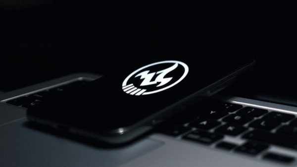 Logo displayed on a phone and laptop screen, dark background.
