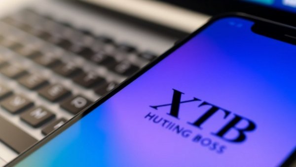 Gratis-Aktie bei XTB, XTB online trading logo on smartphone next to Hugo Boss, vibrant office setting.