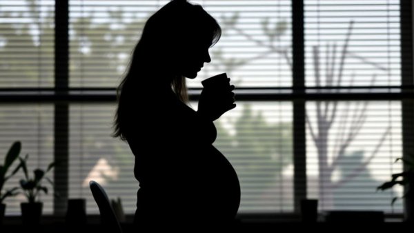 Pregnant woman in office with coffee, silhouette, pregnancy-related leave.