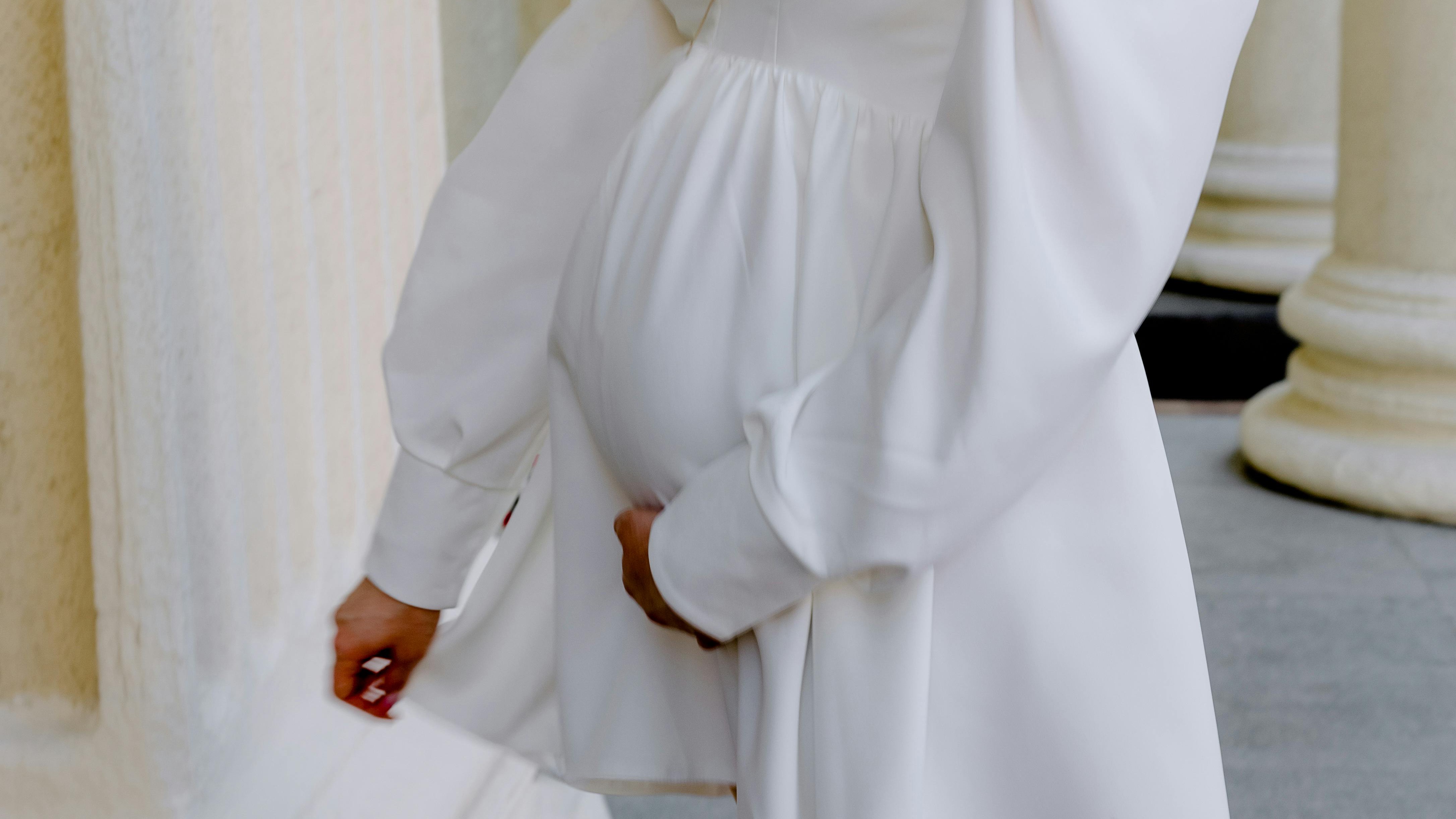 Pregnant woman in white dress receiving gifts at baby shower.