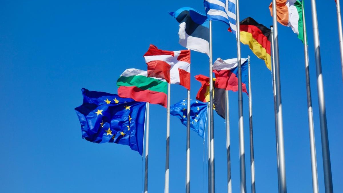 Two individuals rebuilding UK-EU ties, warmly interacting, flags in background.