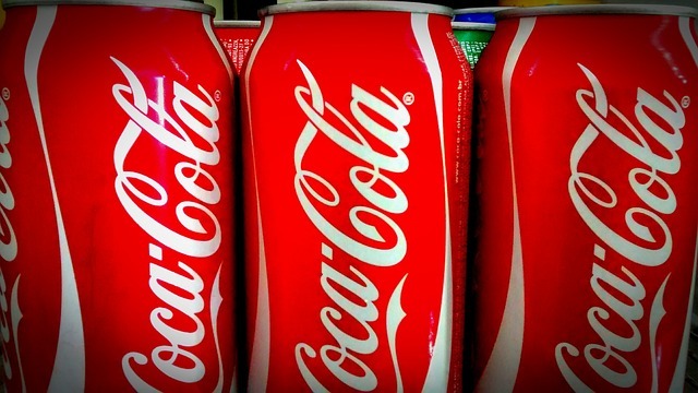 Coca-Cola bottles lined up on a shelf with red caps.