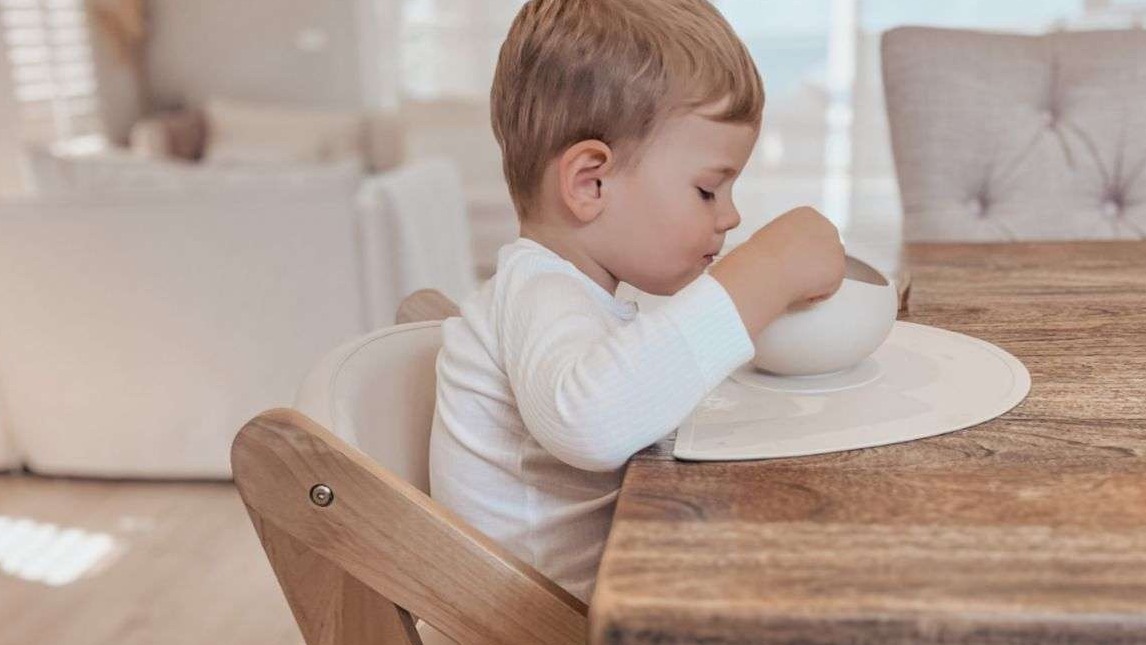 Father feeding baby in portable high chair, cozy home setting.