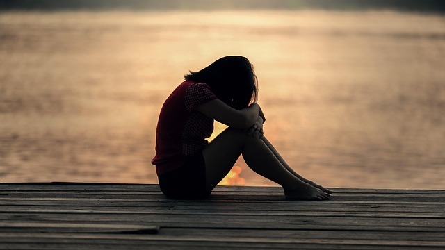 Illustrated daughter's first heartbreak, girl hugging knees, feeling sad.