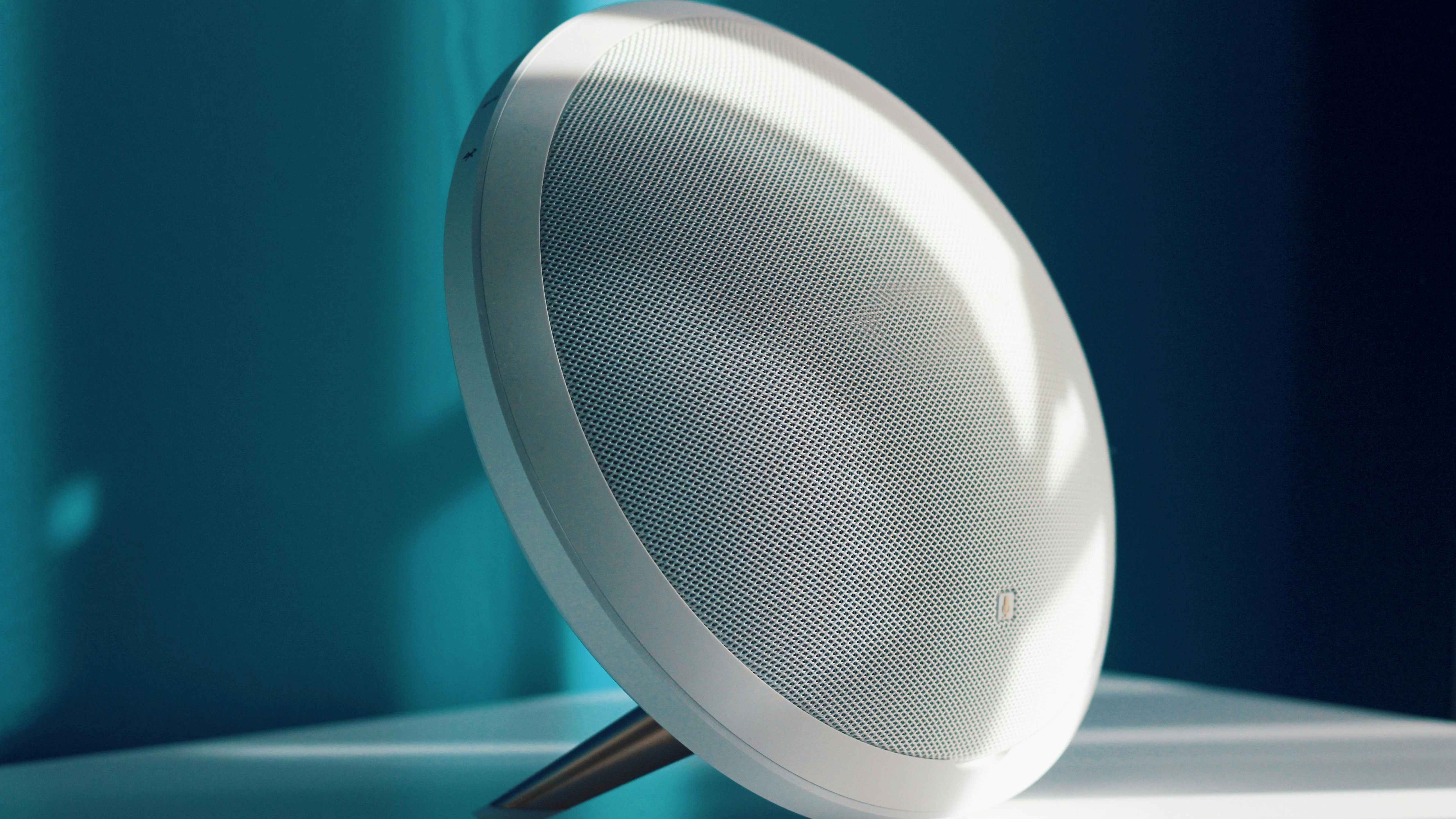 Bluetooth speaker with orange strap on a blue gradient background.