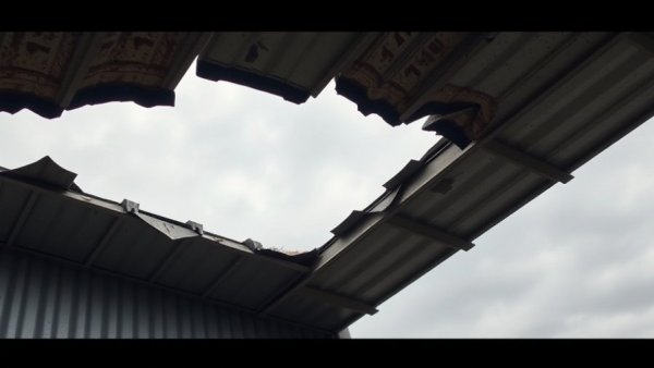Bent metal roof showing damage against a cloudy sky.