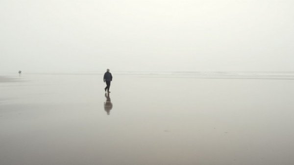 Reflective beach walk under cloudy skies, serene and tranquil.
