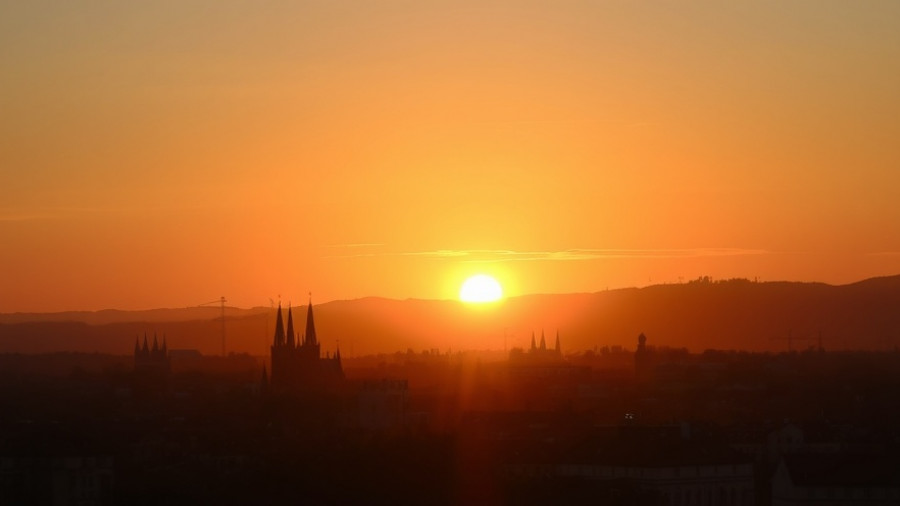 Cityscape silhouette at sunset, warm glow over hills and rooftops.