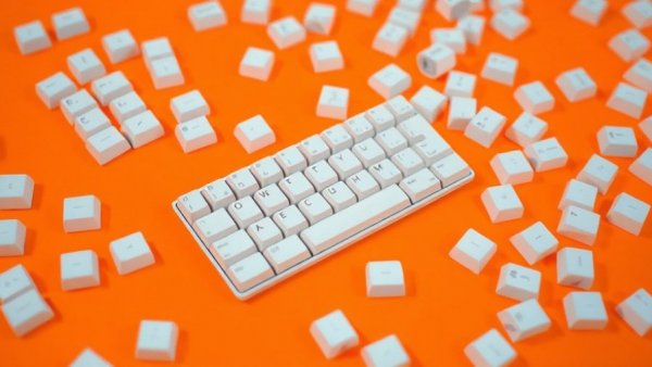 Scattered white keyboard keys on orange surface, symbolizing anthropic challenges before OpenAI IPO.