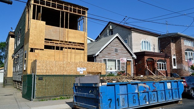 Blue dumpster filled with waste on the street in front of a new house build in a local neighborhoodnd white truck on road, eco-friendly dumpster rentals.