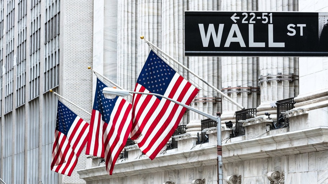 Wall Street sign with American flags in the background, symbolizing economic growth.
