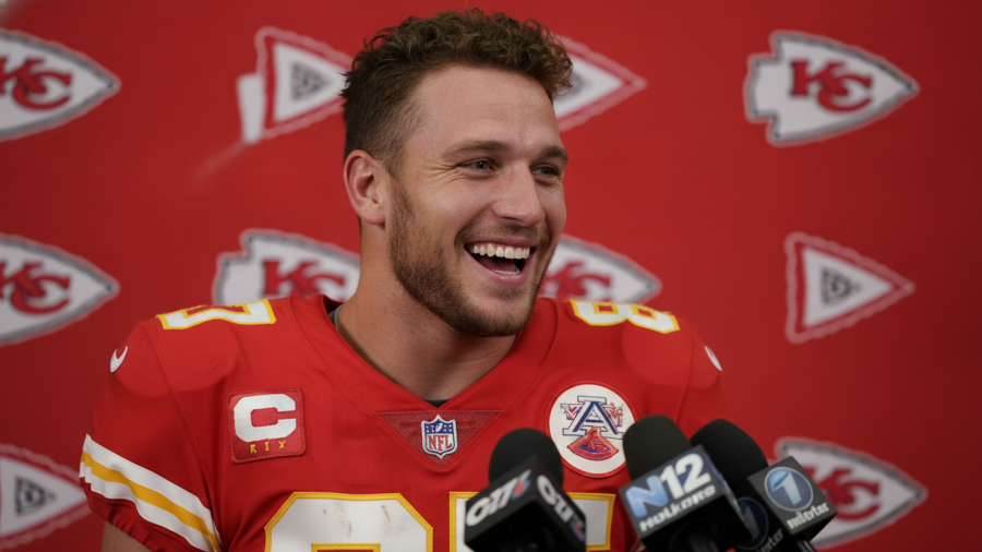 Kansas City Chiefs roster player smiling during media interview, vibrant red backdrop.