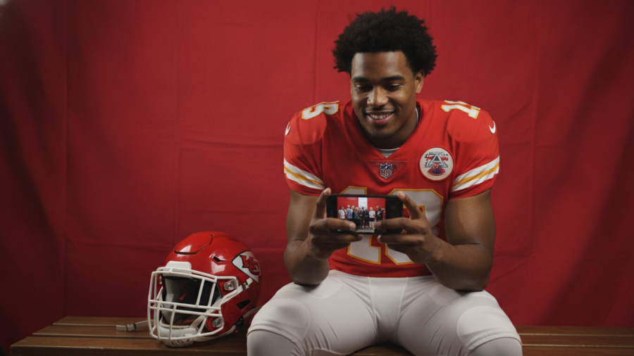 Kansas City Chiefs player on bench with smartphone, showcasing kc chiefs news and rumors.