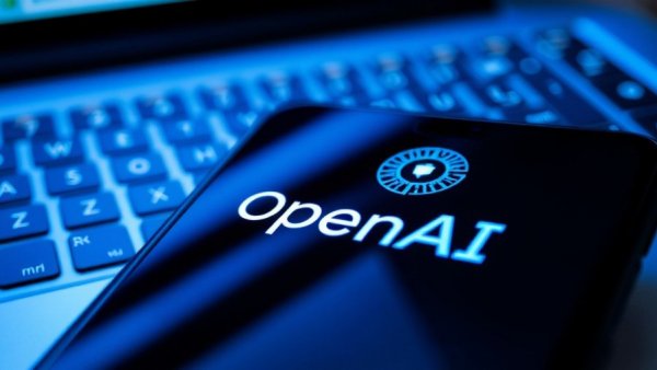 OpenAI logo on phone screen with laptop keyboard, blue lighting.