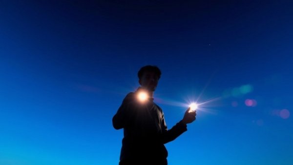 Silhouette holding flashlight with vibrant patterns and bright light.