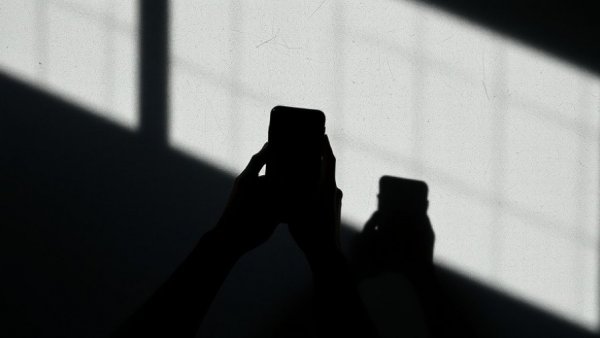 Mystical shadow of hands holding a phone, grey textured backdrop.