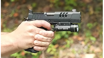 Close-up of handgun features with mini hand model on blurred surface.