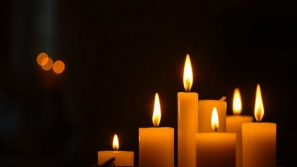 Two glowing candles in dark room, symbolizing remembrance.