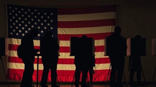 Voters silhouetted against American flag in election setting.