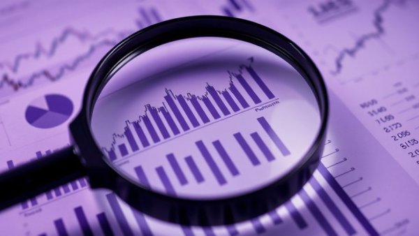 Magnifying glass over financial charts showing economic impact.