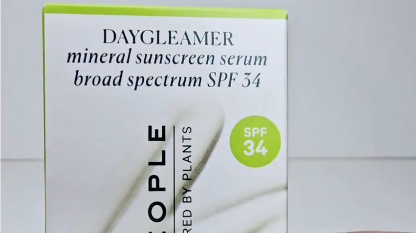 Well People Daygleamer sunscreen bottle amidst green leaves.