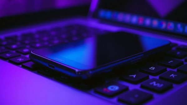 Smartphone on laptop keyboard with colorful lighting, cybercrime concept.